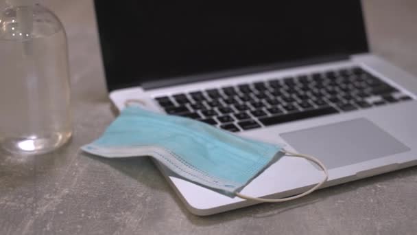 Dator laptop med medicinsk ansiktsmask, anteckningsblock och penna ovanpå det tillsammans med en kopp kaffe på matbordet. Hemma. Begreppet arbete i hemmet. — Stockvideo