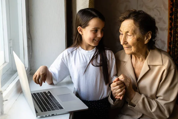 Happy senior woman sitting with her granddaughter looking at laptop making video call. Mature lady talking to webcam, doing online chat at home during self isolation. Family time during Corona — Stock Photo, Image