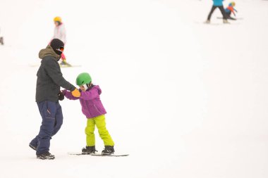 Soğuk Rüzgâr Günü 'nde Dağ Kayağı Tatil Köyü' nde Baba Küçük Kızına Snowboard öğretiyor
