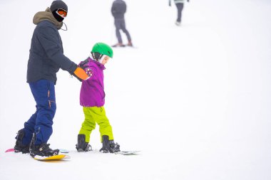Eğitmenler kar yamacındaki bir çocuğa snowboard yapmayı öğretiyor.