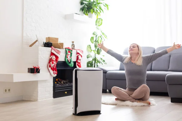 Luchtzuiveraar in een woonkamer, vrouw met laptop met filter voor cleanroom — Stockfoto