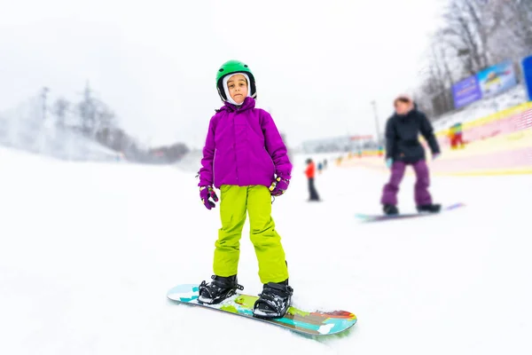 Snowboard Winter Sport. Το κοριτσάκι μαθαίνει σνόουμπορντ, φορώντας ζεστά χειμωνιάτικα ρούχα. Χειμερινό υπόβαθρο. — Φωτογραφία Αρχείου