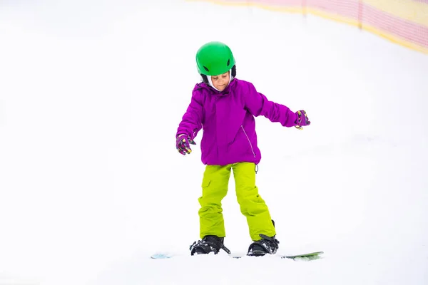 Snowboard Winter Sport. Το κοριτσάκι μαθαίνει σνόουμπορντ, φορώντας ζεστά χειμωνιάτικα ρούχα. Χειμερινό υπόβαθρο. — Φωτογραφία Αρχείου