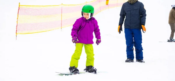 Snowboard Sports d'hiver. petite fille apprenant à faire du snowboard, portant des vêtements chauds d'hiver. Fond d'hiver. — Photo