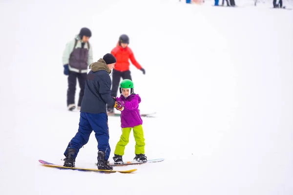 A Hideg Szél Napján a Mountain Ski Resortban Apa tanítja a kicsi lányt snowboardozni — Stock Fotó