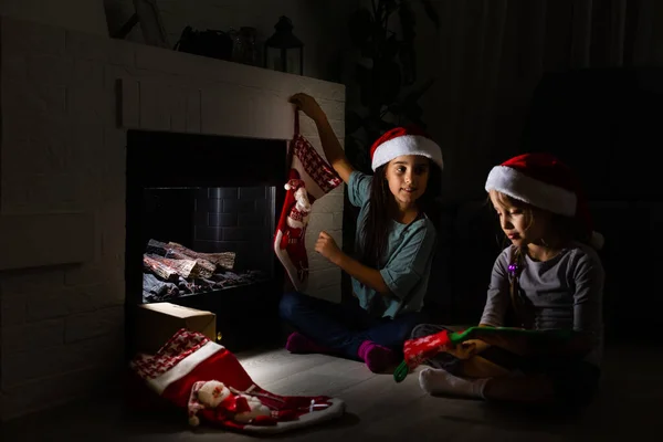 Маленькие дети открывают подарки рядом с камином в уютном доме, празднуя Рождество — стоковое фото