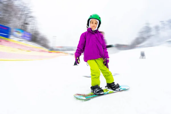 Snowboard Wintersport. kleines Mädchen, das Snowboard lernt und warme Winterkleidung trägt. Winterlicher Hintergrund. — Stockfoto