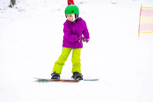 Μικρή χαριτωμένο κορίτσι Snowboarding στο χιονοδρομικό κέντρο στην ηλιόλουστη μέρα του χειμώνα. — Φωτογραφία Αρχείου
