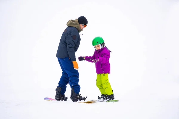 Bei kaltem Winder im Skigebiet bringt Vater seiner kleinen Tochter Snowboarden bei — Stockfoto