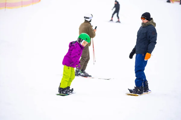 Snowboard Winter Sport. little girl learning to snowboard, wearing warm winter clothes. Winter background.