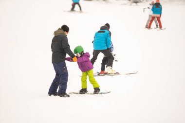 Eğitmenler kar yamacındaki bir çocuğa snowboard yapmayı öğretiyor.