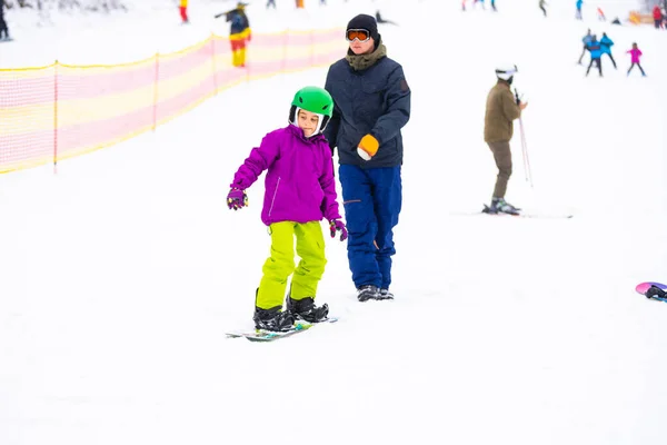 Οι εκπαιδευτές διδάσκουν ένα παιδί σε μια πλαγιά χιονιού να snowboard — Φωτογραφία Αρχείου