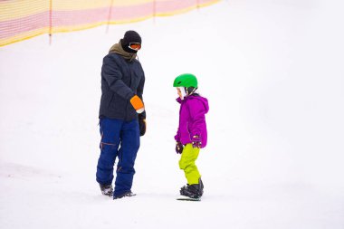Soğuk Rüzgâr Günü 'nde Dağ Kayağı Tatil Köyü' nde Baba Küçük Kızına Snowboard öğretiyor
