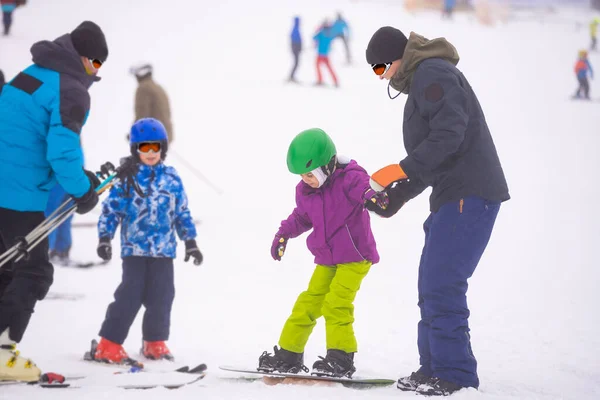 Los instructores enseñan a un niño en una pendiente de nieve a practicar snowboard — Foto de Stock