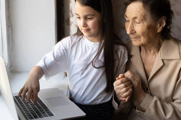 Happy senior woman sitting with her granddaughter looking at laptop making video call. Mature lady talking to webcam, doing online chat at home during self isolation. Family time during Corona — Stock Photo, Image