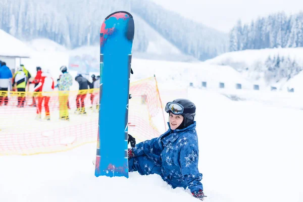 Jovem com snowboard sentado na encosta da colina — Fotografia de Stock