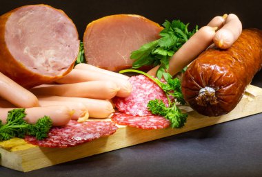 Farklı bir jambon ve salamlı, koyu bir arka planda otlar.