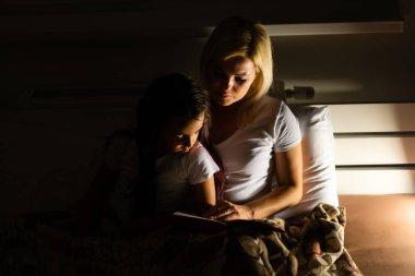 Aile yatmadan önce anne, akşam lambanın yanında çocuk kızına kitap okur.