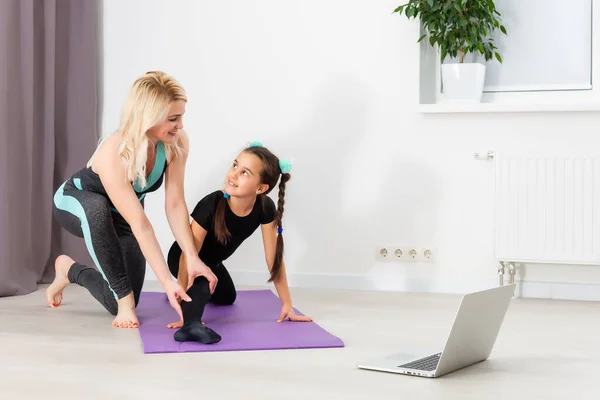 Young mother and daughter are engaged in stretching on a laptop online at home during quarantine or lockdown — Stock Photo, Image