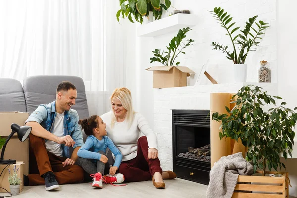 Ευτυχισμένη οικογένεια που κάθεται στο ξύλινο πάτωμα. Πατέρας, μητέρα και παιδί διασκεδάζουν μαζί. Μετακίνηση ημέρα σπίτι, νέα έννοια σπίτι και το σχεδιασμό εσωτερικό — Φωτογραφία Αρχείου