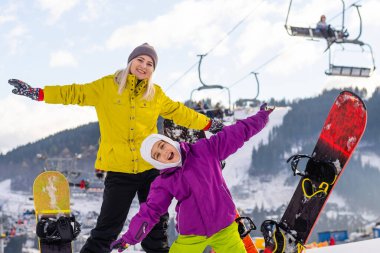 Anne ve kızı kış tatilinde snowboard yapıyor.