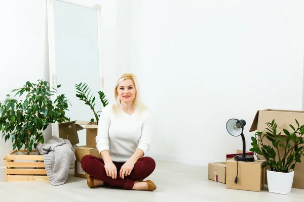 Joyeux jeune femme assise sur le sol près de boîtes mobiles. Une jeune femme déménage chez elle. Femme regardant la caméra et souriant — Photo