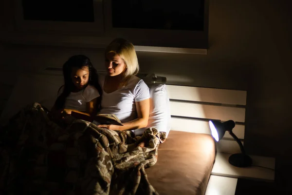 Hora de dormir en familia. Mamá y su hija leyendo un libro en la cama —  Fotos de Stock
