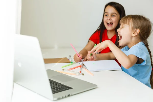 Cool escuela en línea. Los niños que estudian en línea en casa usando un ordenador portátil. Niñas alegres utilizando ordenador portátil estudiando a través del sistema de e-learning en línea. Enseñanza a distancia o remota — Foto de Stock