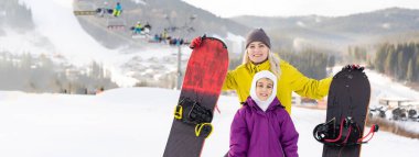 Anne ve kızı kış tatilinde snowboard yapıyor.
