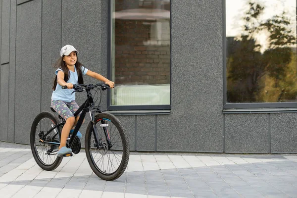 Niña feliz montando una bicicleta en la ciudad — Foto de Stock