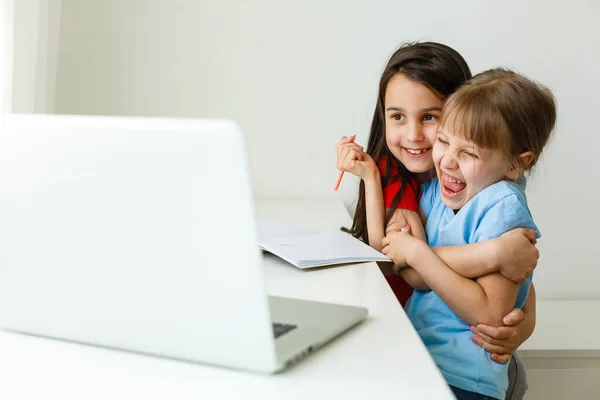 Twee meisjes, de oudste en de jongste, zitten aan een tafel op een laptop. — Stockfoto