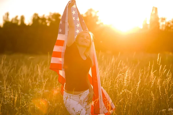 미녀가 호밀 밭에서 바람에 나부끼는 미국 국기를 들고 있어. 푸른 하늘을 배경으로 여름 풍경. 수평 방향. — 스톡 사진