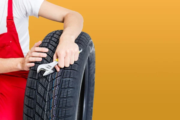Automechanik nesoucí pneumatiky na žlutém pozadí. — Stock fotografie