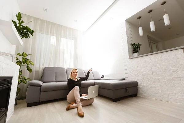 Ung kvinna slår på luftkonditioneringen medan du sitter på soffan nära vit vägg — Stockfoto
