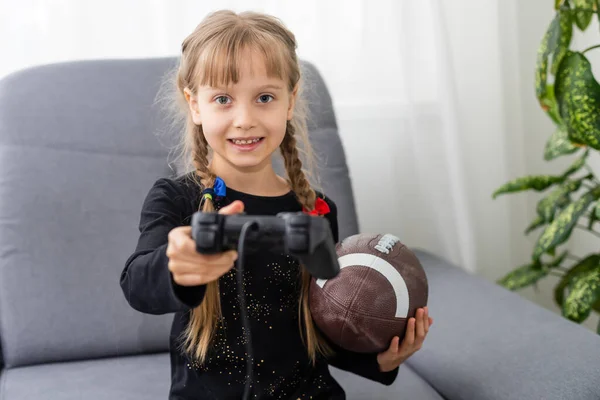 Kleines Mädchen mit Rugby-Ball und Joystick zum Spielen von Videospielen — Stockfoto