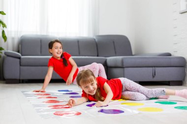 Çocuk kıyafetleri içinde iki mutlu kız yerde coşkuyla oynuyorlar..