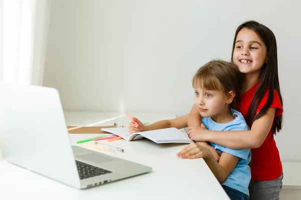 Twee meisjes, de oudste en de jongste, zitten aan een tafel op een laptop. — Stockfoto