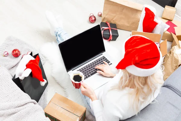Vorbereitungen für die Weihnachtsfeier. Frau bestellt Geschenke und Dekorationen auf Laptop, sitzt zwischen Geschenkboxen und Paketen, kopiert Platz — Stockfoto