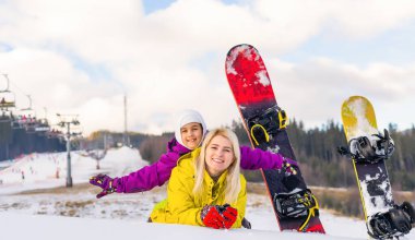 Bir dağ evinde snowboard yapan anne ve kız.
