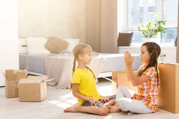 Happy family in living room. Preschool daughters sitting and help unpacking cardboard boxes belongings. Buy real estate, relocation at new modern house