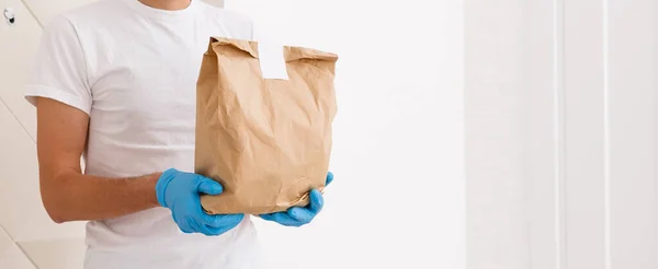 Ung kvinna bär medicinsk mask ta emot paket från leverans inomhus. Förebyggande av virusspridning — Stockfoto