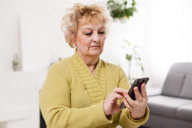 Modern teknolojinin her çağda kolay ve hızlı kullanımı kavramı. Kırışıklıkları olan kendinden emin olgun bir kadının portresi gri arka planda izole edilmiş bir mesaj göndermek için modern akıllı telefonunu kullanıyor.