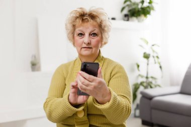 Modern teknolojinin her çağda kolay ve hızlı kullanımı kavramı. Kırışıklıkları olan kendinden emin olgun bir kadının portresi gri arka planda izole edilmiş bir mesaj göndermek için modern akıllı telefonunu kullanıyor.