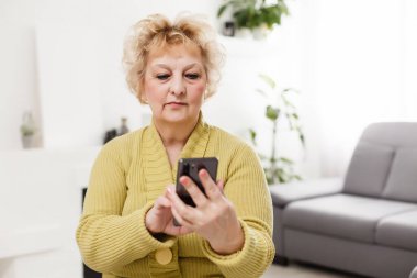 Selfie çekmek ya da görüntülü arama yapmak için dokunmatik ekran cep telefonu kullanan üzgün yaşlı kadın