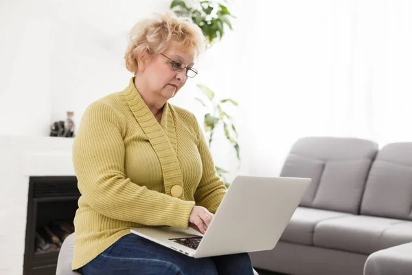 Old woman working on laptop computer at home, Grandma using notebook and searching on internet site