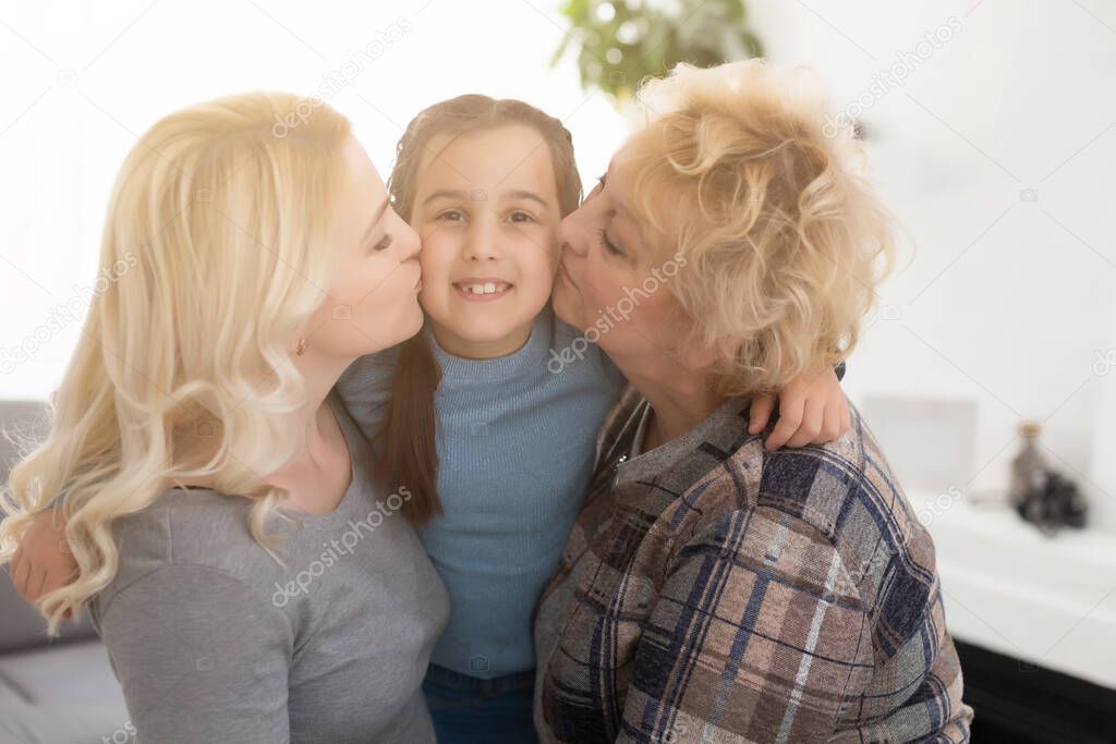 Three generations of women. Beautiful woman and teenage girl are kissing their granny while sitting on couch at home