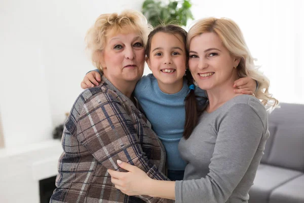 Portrait of three generations of women look at camera posing for family picture, cute little girl hug mom and granny enjoy time at home, smiling mother, daughter and grandmother spend weekend together