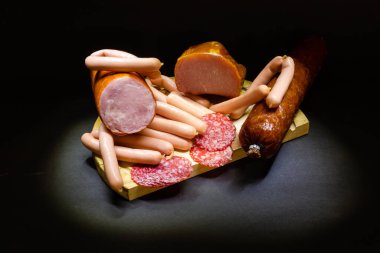 Farklı bir jambon ve salamlı, koyu bir arka planda otlar.