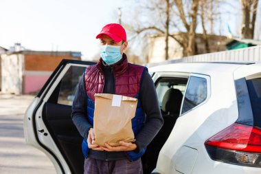 Koruyucu maskeli ve tıbbi eldivenli kurye paket yemek getiriyor. Karantina, hastalık salgını, koronavirüs covid-19 salgını altında teslimat hizmeti.