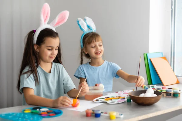 Two happy cute girls sisters paint Easter eggs, oh laugh, show eggs and painted hands — Stock Photo, Image